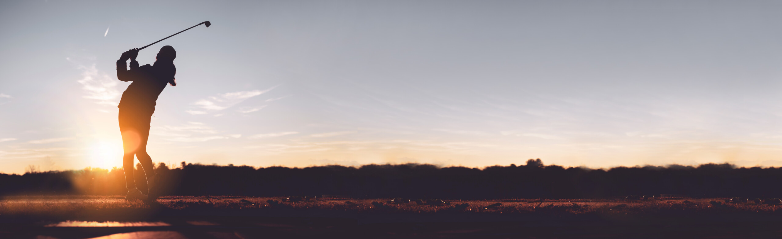 Golferin beim Abschlag im winterlichen Sonnenuntergang